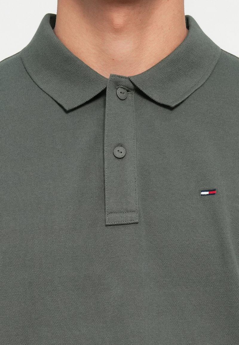 Grijze katoenen poloshirt met een klassieke kraag, twee knopen en een klein geborduurd logo met rode, witte en blauwe accenten op de borst.