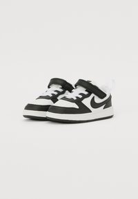 Baskets Nike noires et blanches avec tige en cuir, fermeture à lacets et bande Velcro, bout perforé et semelle en caoutchouc texturée.