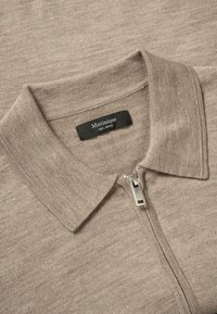 Beige gestricktes Polohemd mit Reißverschluss und einem schwarzen Etikett mit der Aufschrift "Matinique 100% Merino" an der Innenseite des Kragens.