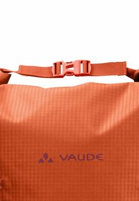 Bolsa de deporte impermeable naranja con una superficie texturizada, que cuenta con una correa ajustable y un cierre central. Logotipo de VAUDE impreso en púrpura.