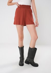 Ruskvärgade shorts gjorda av mjukt tyg med resår i midjan och lös passform, tillsammans med svarta läderstövlar i knähöjd med metallaccenter.