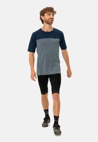 Kortermet, to-tonet skjorte i mørkeblå og grå, kombinert med svarte sykkelshorts og grå fottøy, med mønstrede detaljer på shortsene.