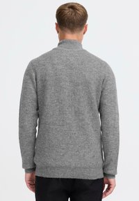 Grijze gebreide trui met een hoge kraag, geribbelde textuur en lange mouwen. De zoom is aan de achterkant iets langer.