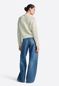 Svetlo rumen pulover z rahlimi pegami in rebrastim zaključkom, združen z modrimi širokimi kavbojkami z visokim pasom in zadnjimi žepi.