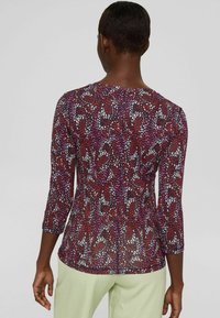 Långärmad topp i flerfärgad abstrakt mönster med röda, lila och vita nyanser. Slät textur med båtskarv och figurnära design.