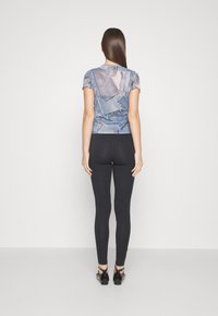 Top corto de manga corta con estampado de denim y mangas rizadas, combinado con leggings negros y zapatos negros, visto desde atrás sobre un fondo liso.