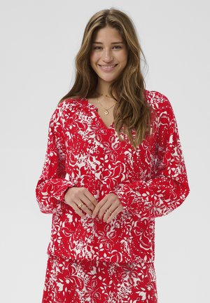 Blouse rouge à imprimé floral avec manches longues, encolure en V et poignets froncés, fabriquée dans un tissu léger et lisse.
