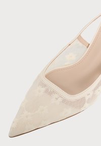 Μπεζ γόβα slingback με μυτερή μύτη, λεπτό διακοσμητικό δίχτυ με λουλούδια και λείο δερμάτινο περίγραμμα στο πάνω μέρος.