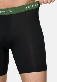 Schwarze Baumwoll-Boxershorts mit einem grünen elastischen Taillenbund, auf dem der Text "Phil & Co." in Weiß aufgedruckt ist. Glatte Textur, körperbetonter Schnitt.