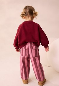 Maronfarvet oversized sweatshirt og pink stribede bukser, der har brede ben og to baglommer, parret med brune ankelstøvler.