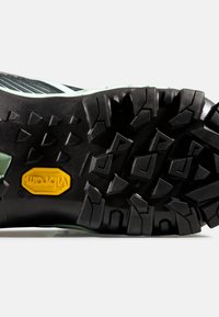 Suola in gomma nera con un motivo di battistrada profondo e testurizzato. Logo giallo Vibram visibile in una sezione centrale. Accenti verde menta lungo i bordi.