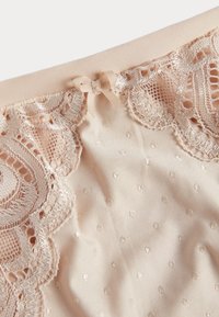 Beige stof met kantaccent, voorzien van een gestippelde textuur en een klein lintstrikje. Glad materiaal met een delicaat geborduurd randje.
