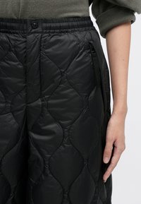 Juodi siuvinėti kelnių kelnaičiai su blizgiu, lygiu paviršiumi. Turi elastingą juosmenį ir šonines kišenes su diskretiškais užtrauktukais.