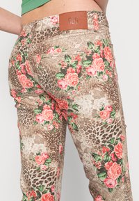 Calças de ganga estampadas com flores em castanho, com rosas cor-de-rosa e detalhes de leopardo. Apresentam um rótulo de couro na cinta e um tecido texturizado.