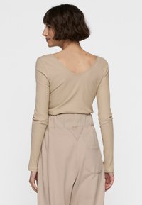 Beige, geripptes langärmliges Oberteil mit tiefem V-Ausschnitt auf der Rückseite, kombiniert mit lockeren, hellbeigen Hosen, die eine Gesäßtasche und eine weiche Stofftextur aufweisen.
