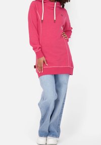 Felpa rosa con cappuccio e vestibilità comoda, caratterizzata da cuciture bianche, cordini e un piccolo logo. Abbinata a jeans a gamba larga di colore blu chiaro.