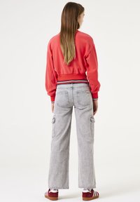 Sudadera corta roja con puños y cintura acanalados, combinada con pantalones cargo de pierna ancha en gris que cuentan con bolsillos laterales y una textura desgastada.