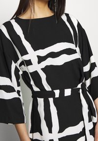 Abito a righe bianche e nere con vestibilità ampia, maniche larghe e vita con cintura. Presenta strisce astratte audaci su un tessuto liscio.