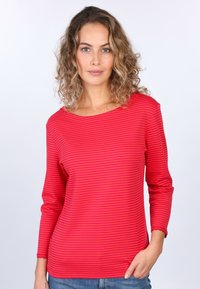 Rot und hellrosa gestreifte Bluse mit langen Ärmeln, weitem Ausschnitt und gewelltem Saum, aus weichem Stoff, kombiniert mit blauen Jeans.