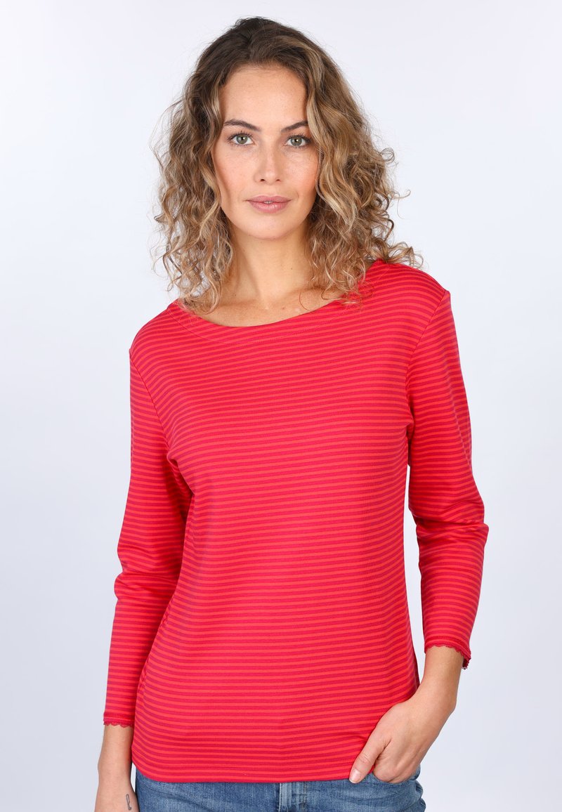 Rot und hellrosa gestreifte Bluse mit langen Ärmeln, weitem Ausschnitt und gewelltem Saum, aus weichem Stoff, kombiniert mit blauen Jeans.