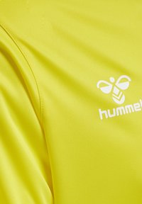 Lys gul sportsjersey lavet af glat stof, med det hvide "hummel" logo og et bi ikon på venstre brystområde.
