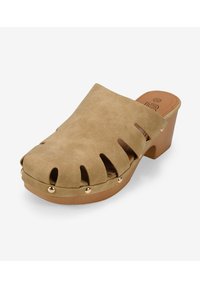 Zuecos de ante sintético color beige con detalles recortados, punta redondeada y tacón grueso. Los remaches en tono dorado a lo largo de la suela añaden un toque de detalle.