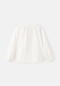 Blouse blanche à manches longues avec un col rond. Tissu texturé avec des plis et une fermeture à boutons dans le dos. Conception douce et légère.