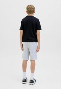 T-shirt nera a maniche corte, pantaloni corti grigi, calzini bianchi e scarpe da ginnastica nere. Design semplice; texture liscia; vestibilità casual.