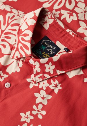 Camicia di cotone rossa con motivi floreali bianchi, colletto con bottoni e etichetta "Superdry". Tessuto morbido con finitura liscia.