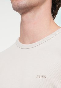 Ελαφρώς μπεζ πλεκτό πουλόβερ με στρογγυλή λαιμόκοψη, με υφασμάτινη υφή και διακριτικό λογότυπο "BOSS", με ριμπ λαιμόκοψη και λείο φινίρισμα.