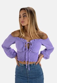 Blouse violette à épaules dénudées avec un col à volants et un corps froncé. Des manches longues bouffantes complètent le design ajusté.