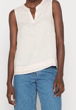 Leinen ärmelloses Top in hellem Beige mit V-Ausschnitt und geschichtetem Saumdetail. Kombiniert mit hoch taillierten blauen Denim-Jeans.