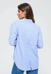 Chemise à rayures bleues et blanches avec col, manches longues et hem arrondi, dotée d'une fermeture à boutons au dos.