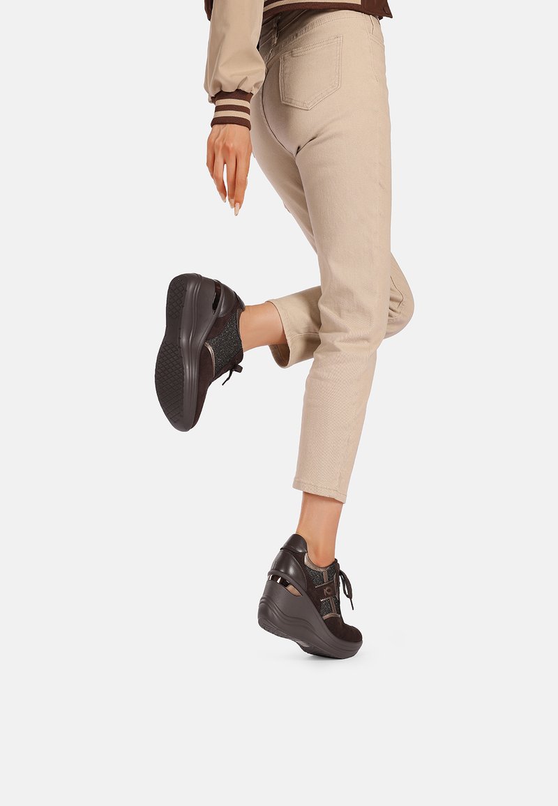 Sneakers a zeppa neri e marroni con tessuto testurizzato, chiusura con lacci e accenti ritagliati, abbinati a pantaloni cropped beige chiaro.