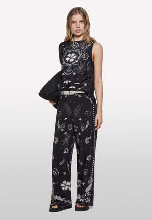Outfit nero composto da un top senza maniche e pantaloni a gamba larga con motivi floreali bianchi. Include una borsa nera intrecciata e una cintura texturizzata.