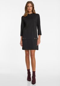 Zwart gestreepte jurk met een hoge hals, driekwartmouwen en gouden accenthardware aan de zoom. Gladde textuur, knielange ontwerp.