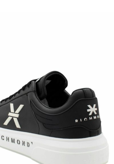 Sneaker in pelle nera con dettagli in logo e testo bianchi. Presenta una punta arrotondata, suola piatta e texture liscia. Design con tacco elevato.