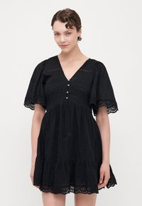 Schwarzes Baumwollkleid mit kurzen Puffärmeln, V-Ausschnitt, Spitzenverzierungen und dekorativen Knöpfen. Verfügt über einen gestuften Rock mit bestickten Akzenten.
