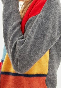 Strickpullover mit grauem Körper, rotem Kragen und bunten geometrischen Panele in Blau, Gelb und Orange mit angenehmer Textur.