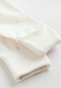 Gros plan sur des manches en tissu blanc côtelé avec poignets, présentant de fines taches roses sur un fond clair.