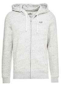 Felpa con zip color grigio chiaro realizzata in tessuto di pile testurizzato. Presenta un cappuccio con coulisse, tasche a marsupio e un piccolo logo sul petto.