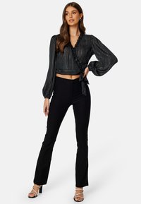 Blusa nera corta avvolgente con bordo arricciato e strisce verticali argentate, abbinata a pantaloni neri a zampa e tacchi a strappo.
