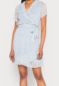 Vestido envolvente azul claro con mangas cortas con volantes, que presenta un patrón floral y una cintura ceñida con cinturón. Hecho de una tela ligera y texturizada.