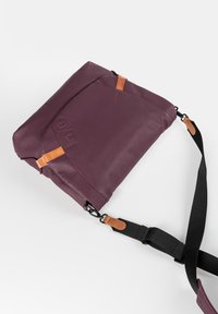 Borsa a tracolla piegata di colore viola scuro con tracolla nera regolabile e dettagli in pelle beige su sfondo bianco semplice.