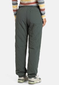Gequiltte groene broek met een relaxte pasvorm, elastische tailleband en een achterzak, gecombineerd met neutrale sneakers. Textuurdetails zichtbaar.