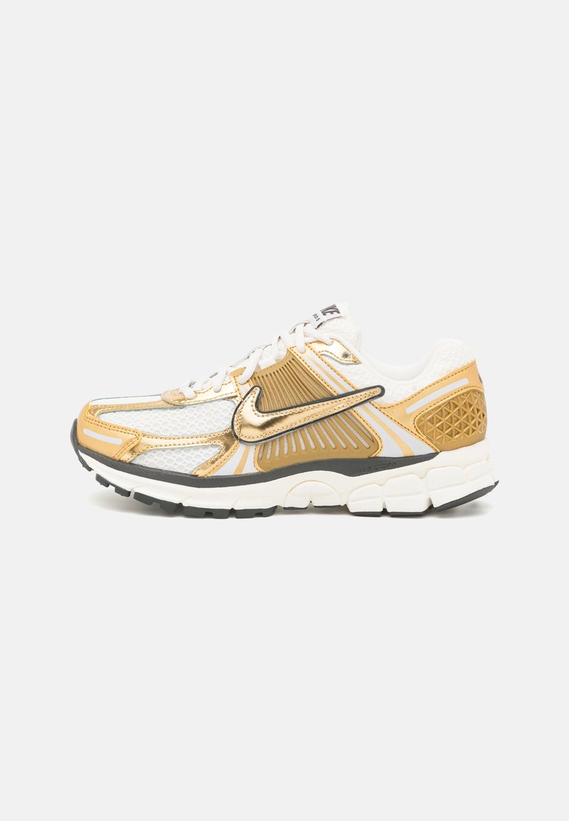 Nike running shoe featuring a predominantly white mesh upper with gold and gray accents, a padded collar, and a textured black sole.