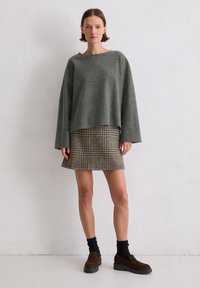 Grijze wollen trui met brede mouwen, gecombineerd met een minirok in bruin houndstooth, en donkere sokken met brown instapschoenen.