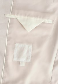 Heller beiger Stoff mit glatter Textur verfügt über eine dreieckige Klappe und ein quadratisches Patch. Die Kanten haben eine weiße Paspelierung.