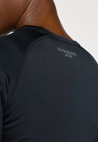 Juoda aktyvaus dėvėjimo palaidinė su apvalia iškirpte, lygiu tekstūra ir kontrastingomis siūlėmis. Ant nugaros matomas prekės ženklo „even&odd ACTIVE“ pavadinimas.