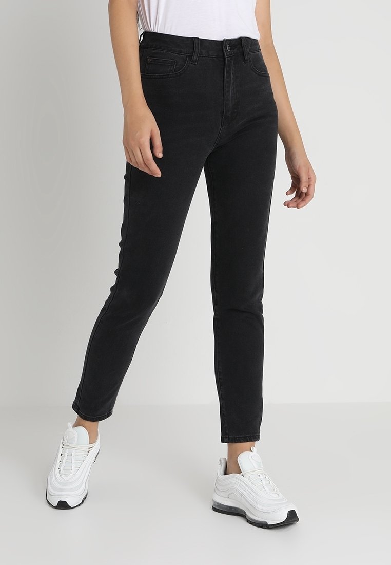 Jeans de mezclilla negros con corte ajustado, diseño de cinco bolsillos y detalles de costura sutiles. Combinados con zapatillas blancas para un contraste.